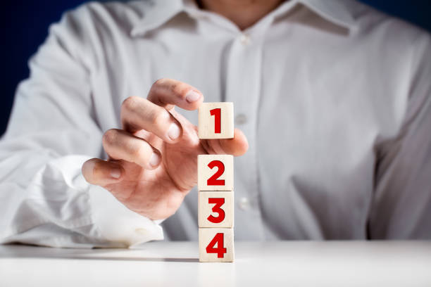 Businessman hand puts a wooden block with the number one on top of the tiered cubes. First step, level or rank stock photo