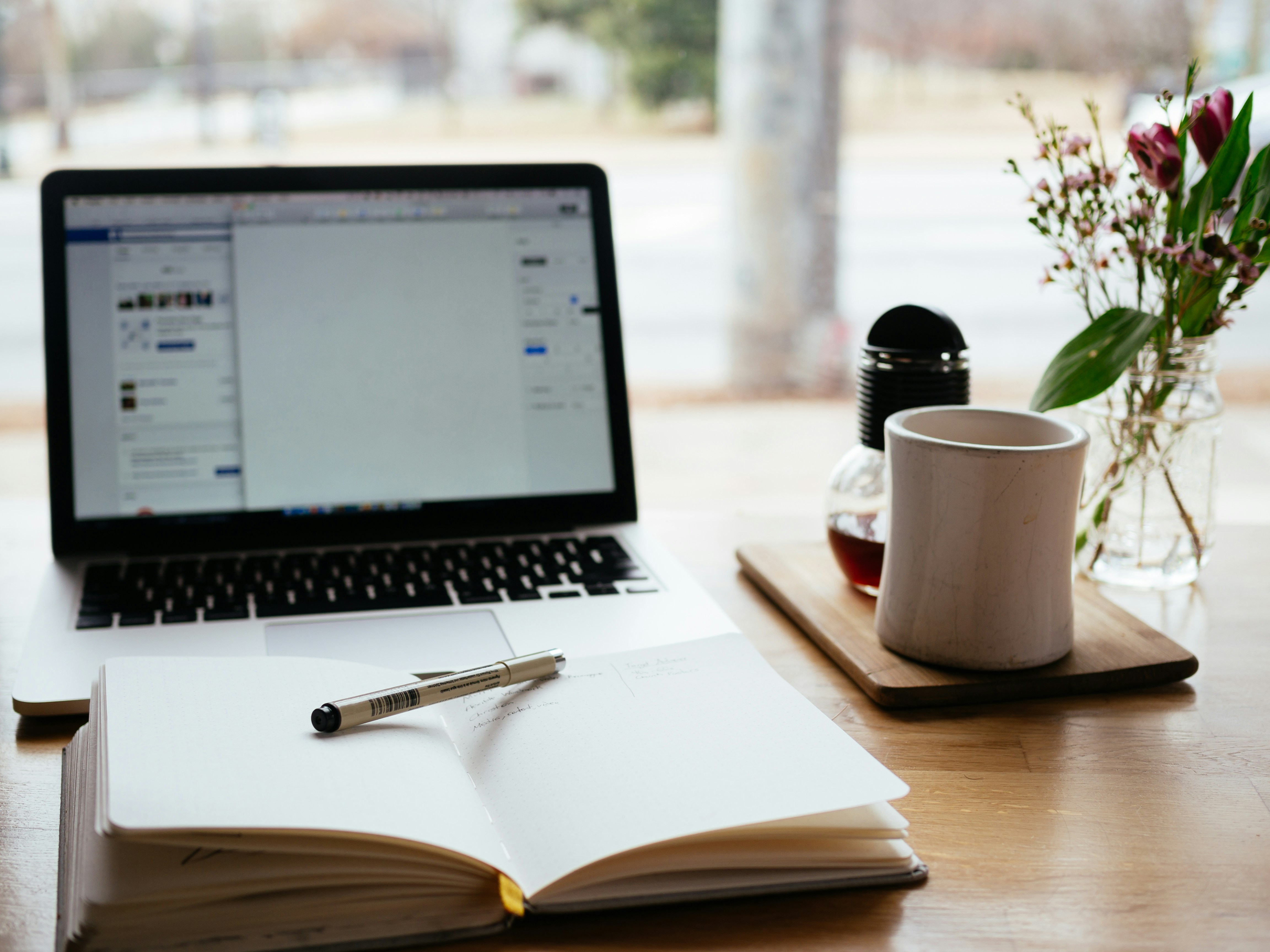 Open notebook and pen beside a mug and an open laptop